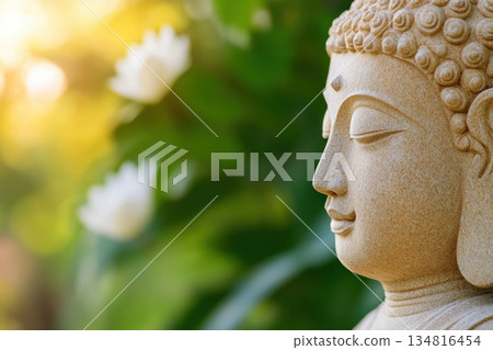 Intricately carved stone Buddha statue surrounded by lotus flowers in a lush garden bathed in gentle morning sunlight Intricately carved stone Buddha statue surrounded by lotus flowers in a lush garden bathed in gentle morning sunlight 134816454