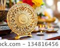 Intricately carved golden Dharma Wheel on an altar surrounded by incense and candles in a serene Buddhist setting 134816456