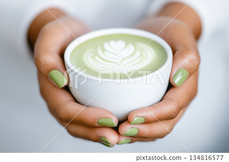 Close-up of womans hands with sage green nail polish holding a delicate ceramic cup filled with matcha tea in a serene and minimalistic setting Close-up of womans hands with sage green nail polish holding a delicate ceramic cup filled with matcha tea in a serene and minimalistic setting 134816577