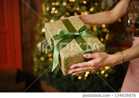 Unrecognizable woman holds a wrapped gift in front of a decorated tree during a holiday gathering Unrecognizable woman holds a wrapped gift in front of a decorated tree during a holiday gathering 134816878