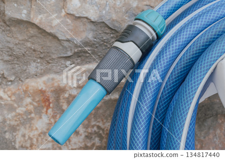 Garden hose with spray nozzle on holder by stone wall Garden hose with spray nozzle on holder by stone wall 134817440