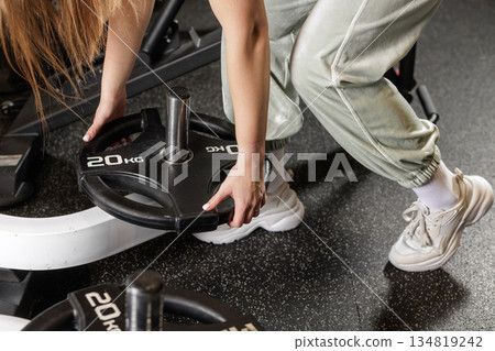 Close up of female hands loading weight plate on barbell preparing for powerlifting strength training in modern gym Close up of female hands loading weight plate on barbell preparing for powerlifting strength training in modern gym 134819242