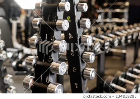 Closeup of dumbbells on rack in modern gym interior representing strength training workout and fitness equipment concept Closeup of dumbbells on rack in modern gym interior representing strength training workout and fitness equipment concept 134819293