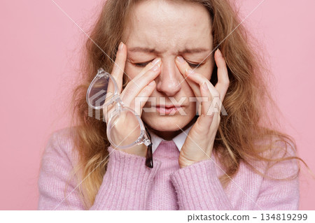 Close up portrait of woman holding glasses and pressing eye corners showing migraine sinus pressure and vision discomfort concept Close up portrait of woman holding glasses and pressing eye corners showing migraine sinus pressure and vision discomfort concept 134819299