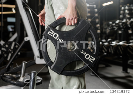 Close up of female athlete holding weight plate in fitness club while setting up equipment for strength workout 134819372