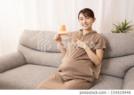 An eight-month pregnant woman sitting on a sofa and holding a bankbook An eight-month pregnant woman sitting on a sofa and holding a bankbook 134819446