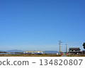 Under a cloudless blue sky, a Kiha 40 train travels through a tranquil rural landscape. 134820807