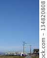Under a cloudless blue sky, a Kiha 40 train travels through a tranquil rural landscape. 134820808