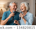 Elderly man and woman singing karaoke together in a cozy modern living room 134820815