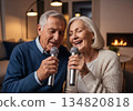 Elderly man and woman singing karaoke together in a cozy modern living room 134820818