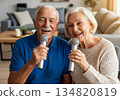 Elderly man and woman singing karaoke together in a cozy modern living room 134820819