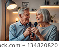 Elderly man and woman singing karaoke together in a cozy modern living room 134820820