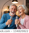 Elderly man and woman singing karaoke together in a cozy modern living room 134820822
