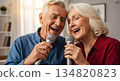 Elderly man and woman singing karaoke together in a cozy modern living room 134820823