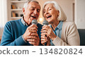 Elderly man and woman singing karaoke together in a cozy modern living room 134820824