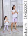 Mother and daughter standing in prayer pose, meditating on yoga mat indoors 134822202