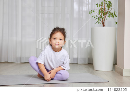 Young girl practices wellness, sitting on a yoga mat in a bright room 134822205