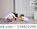 Mother helping young daughter stretching on a yoga mat during home workout 134822206