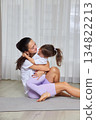 Happy mother hugging smiling daughter during home fitness on a yoga mat 134822213
