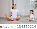 Mother and daughter sitting in lotus pose on yoga mats at home 134822214