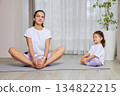 Mother and daughter practicing yoga poses on a mat in their living room 134822215