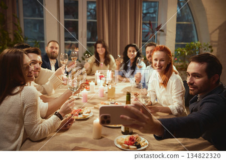 Friends raising wine glasses for group selfie at dinner. Friends raising wine glasses for group selfie at dinner. 134822320