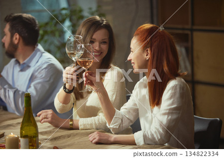 Women clinking wine glasses sitting at dinner table with candles and food. Women clinking wine glasses sitting at dinner table with candles and food. 134822334