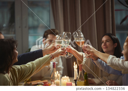 Group of people raising wine glasses for toast during home dinner 134822336