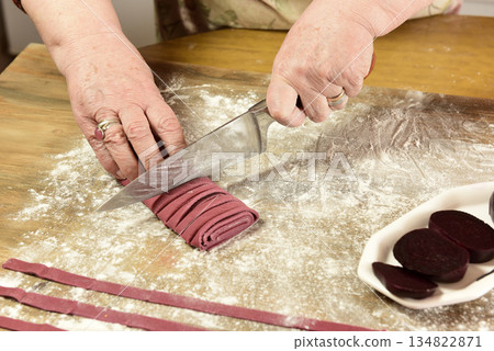 Hands cutting purple noodles with ingredients on the table, homemade italian food. Hands cutting purple noodles with ingredients on the table, homemade italian food. 134822871