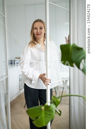 Woman in white shirt opening door in bright minimalist home interior Woman in white shirt opening door in bright minimalist home interior 134824278