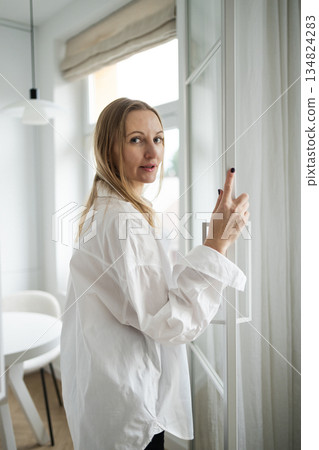 Woman in white shirt spraying perfume at home near window 134824283