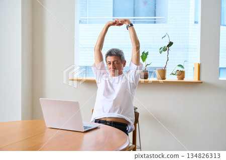 一位老年男子正在伸展身體，使用電腦，在家辦公，遠距辦公 134826313