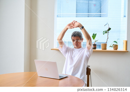 一位老年男子正在伸展身體，使用電腦，在家辦公，遠距辦公 134826314