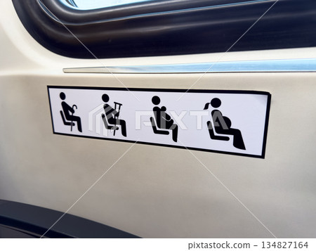 Black signs on white sticker next to seat on public vehicle indicate seats for people with difficulty standing. Give up your seat to elderly person, pregnant woman, or passenger with child 134827164