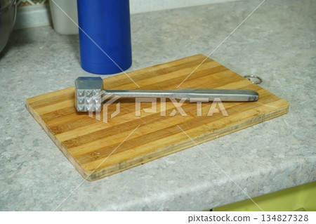 Iron meat mallet lies on a kitchen wooden board 134827328