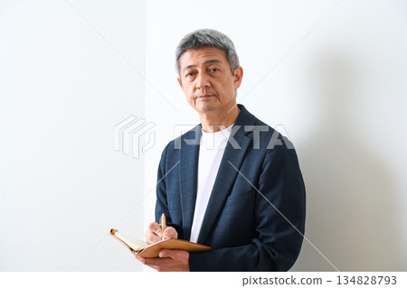 A senior man wearing a jacket and taking notes in his notebook A senior man wearing a jacket and taking notes in his notebook 134828793