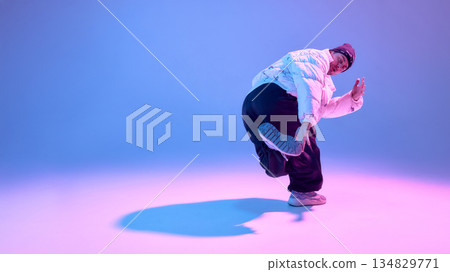Street dancer performing dynamic pose in studio with colored light. 134829771