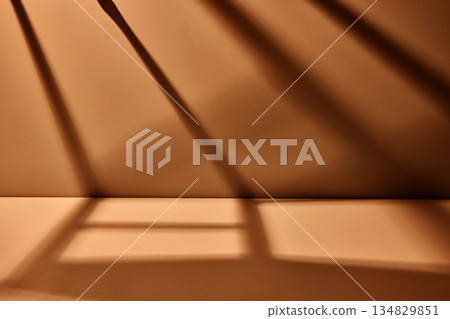Warm brown studio background with dramatic diagonal light shadows creating minimal cinematic scene with strong depth and copy space 134829851