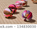 A single temari ball placed on a tatami mat and a string of temari balls in the background | A Japanese still life that highlights the main subject 134830030