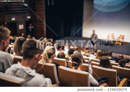 Speaker giving a talk in conference hall at business event. Rear view of unrecognizable people in audience at the conference hall. Business and entrepreneurship concept Speaker giving a talk in conference hall at business event. Rear view of unrecognizable people in audience at the conference hall. Business and entrepreneurship concept 134830074
