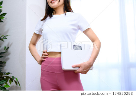 Smiling Japanese woman in yoga wear holding a weight scale Diet leggings 134830298
