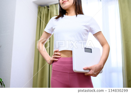 Smiling Japanese woman in yoga wear holding a weight scale Diet leggings Smiling Japanese woman in yoga wear holding a weight scale Diet leggings 134830299