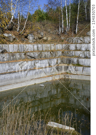 Huge geometric stone shapes and autumn birches reflected in the water of the abandoned marble quarry Huge geometric stone shapes and autumn birches reflected in the water of the abandoned marble quarry 134830703