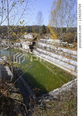 Huge geometric stone shapes and autumn birches reflected in the water of the abandoned marble quarry Huge geometric stone shapes and autumn birches reflected in the water of the abandoned marble quarry 134830704