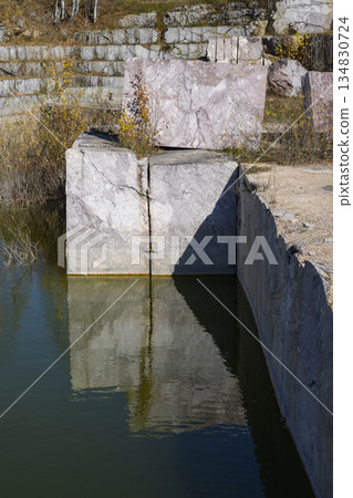 Huge cubic and geometric stone shapes are reflected in the water of the abandoned marble quarry 134830724