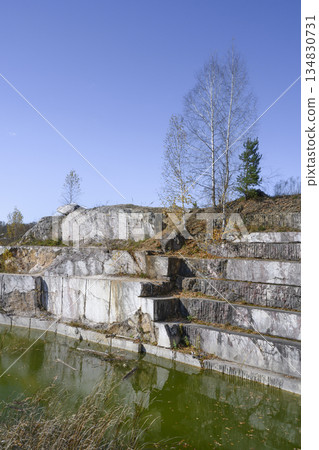 Huge geometric stone shapes and autumn birches reflected in the water of the abandoned marble quarry 134830731