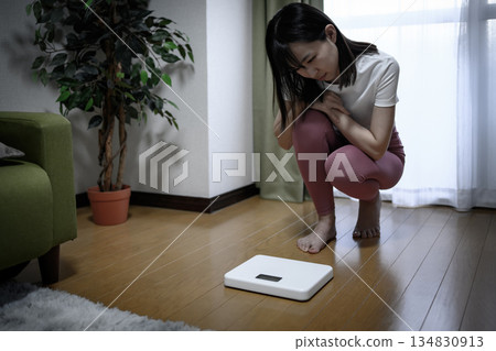 一位身穿瑜珈服的日本女性正在查看體重計、飲食、緊身褲和顏色減淡情況。 134830913