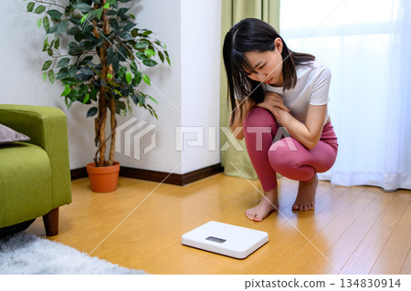 身穿瑜珈服的日本女子正在檢查體重計、飲食和緊身褲。 身穿瑜珈服的日本女子正在檢查體重計、飲食和緊身褲。 134830914