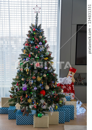 Artificial Christmas tree with colorful ornaments and wrapped gifts in bright living room Artificial Christmas tree with colorful ornaments and wrapped gifts in bright living room 134831331