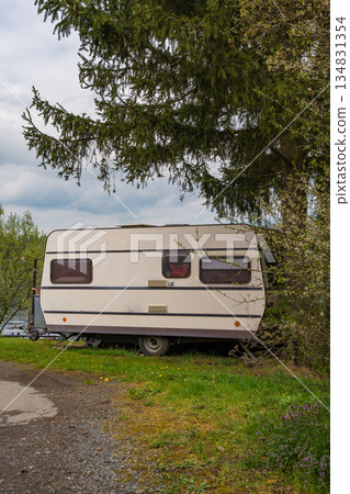 Vintage caravan parked near river under fir tree - peaceful spring camping scene in rural nature 134831354